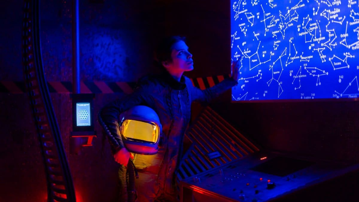 Astronaut in space suit analyzing a futuristic star map in a dimly lit chamber.