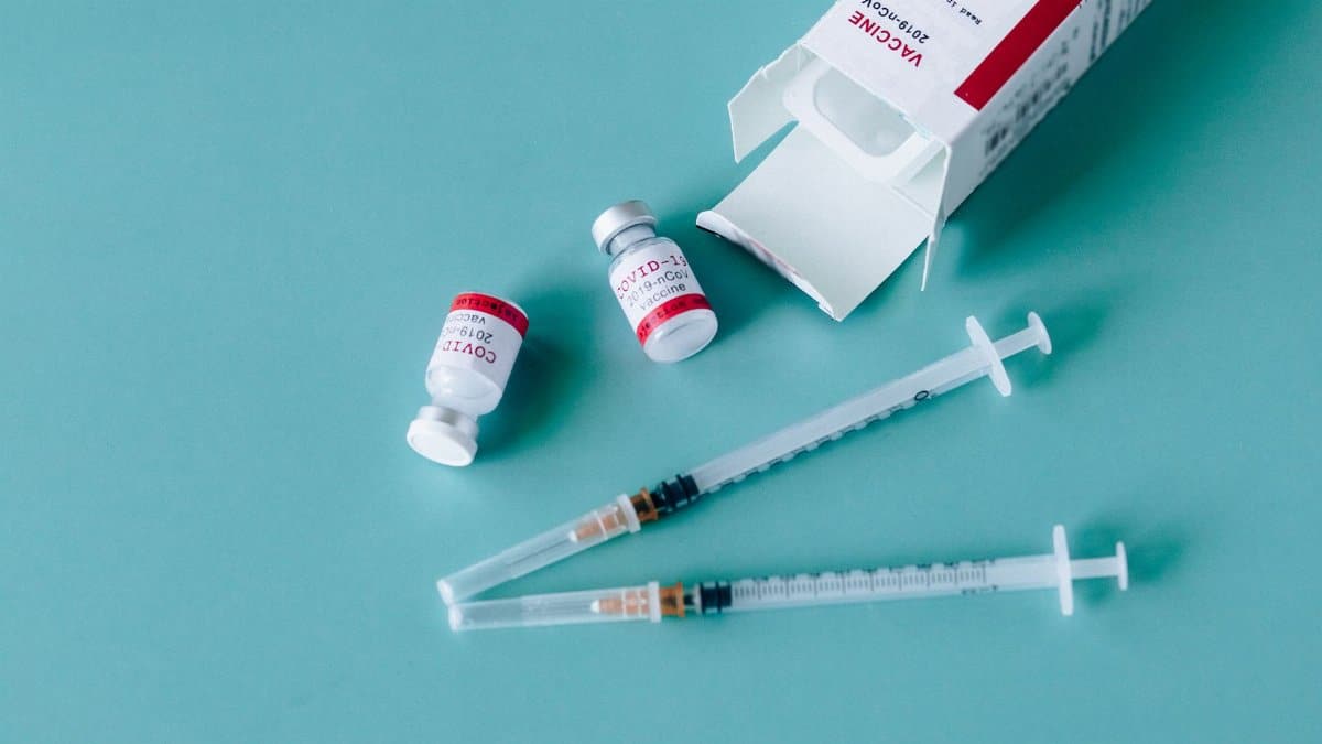Close-up of COVID-19 vaccine vials and syringes on a blue surface, symbolizing vaccination efforts.