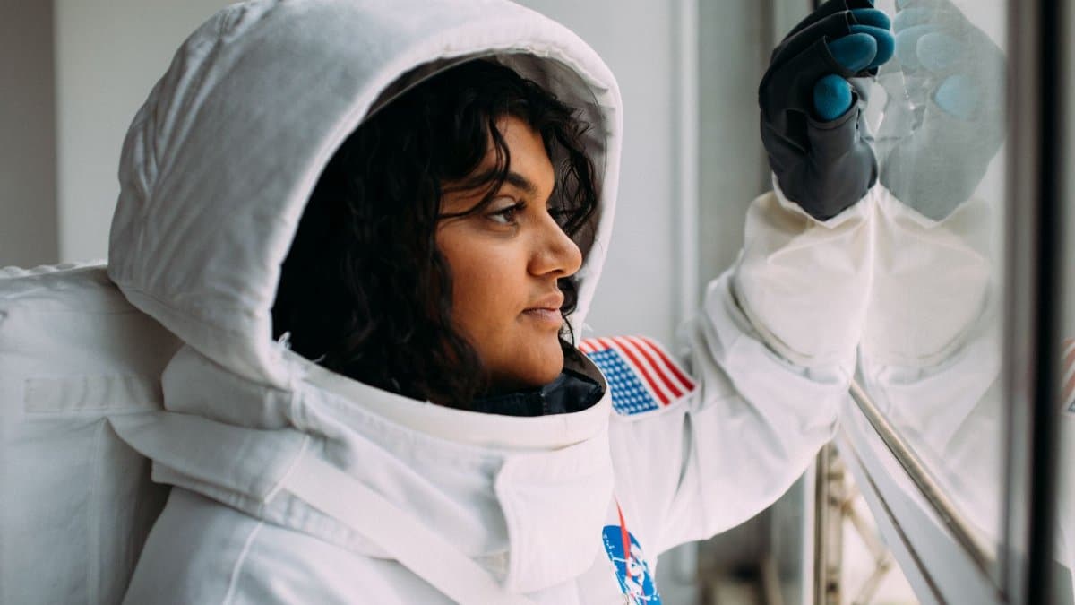 A woman in an astronaut suit looks thoughtfully out of a window, embodying space exploration dreams.