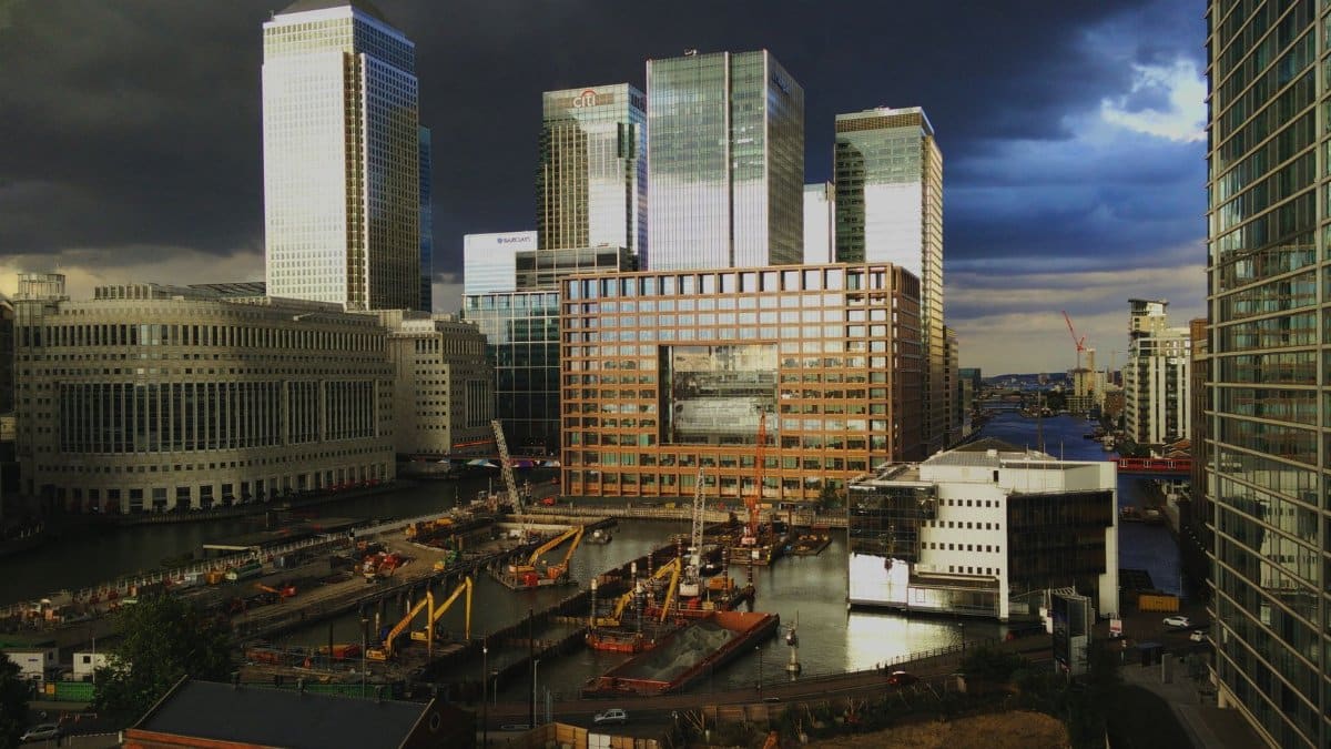 A dramatic scene of Canary Wharf skyscrapers and construction site against a dark, stormy sky.