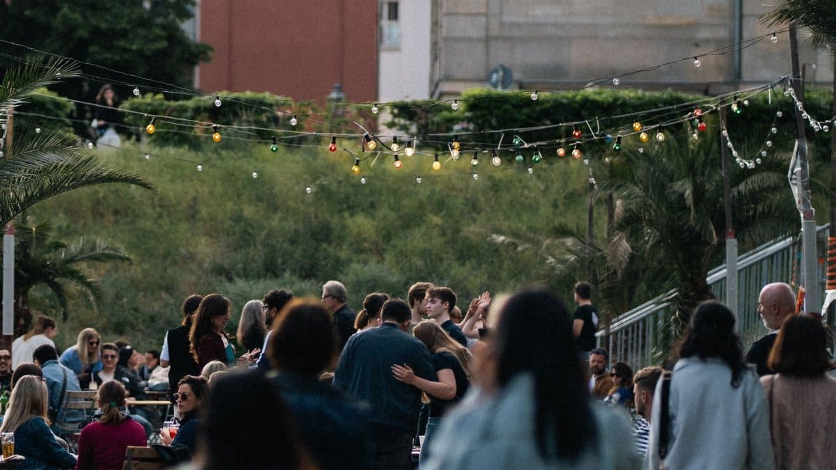 Enjoy a lively outdoor gathering with colorful lights and a diverse crowd at dusk in an urban setting.