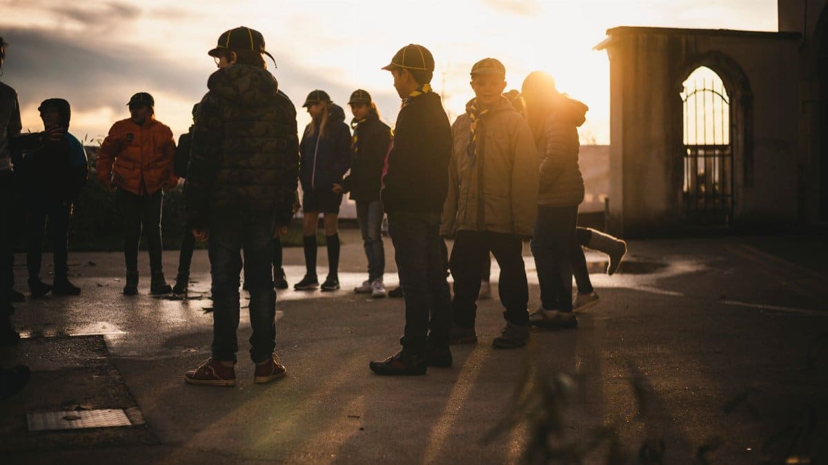 A group of children stands together outdoors at sunset, enjoying the golden hour.