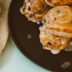 Close-up view of freshly baked cinnamon rolls drizzled with icing on a black plate.