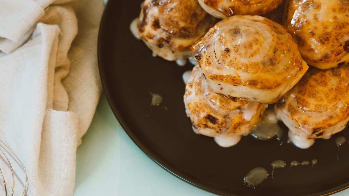 Close-up view of freshly baked cinnamon rolls drizzled with icing on a black plate.