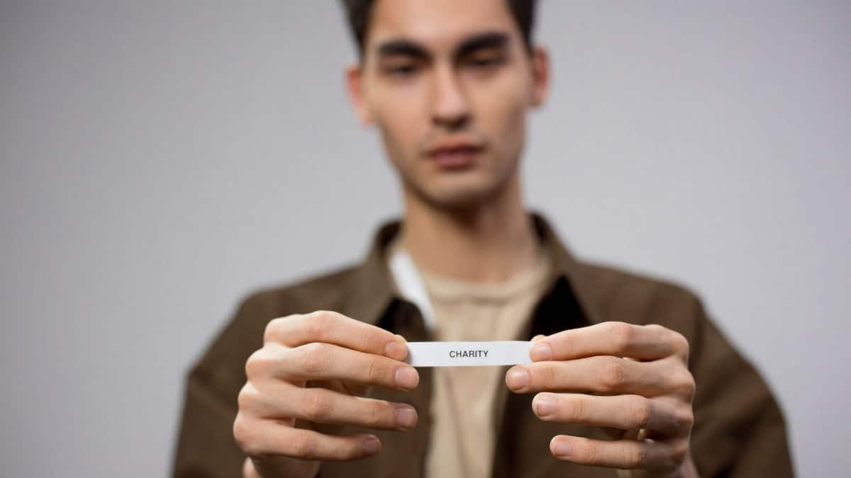 A man holds a note reading 'charity,' with the focus on his hands, expressing a charitable theme.