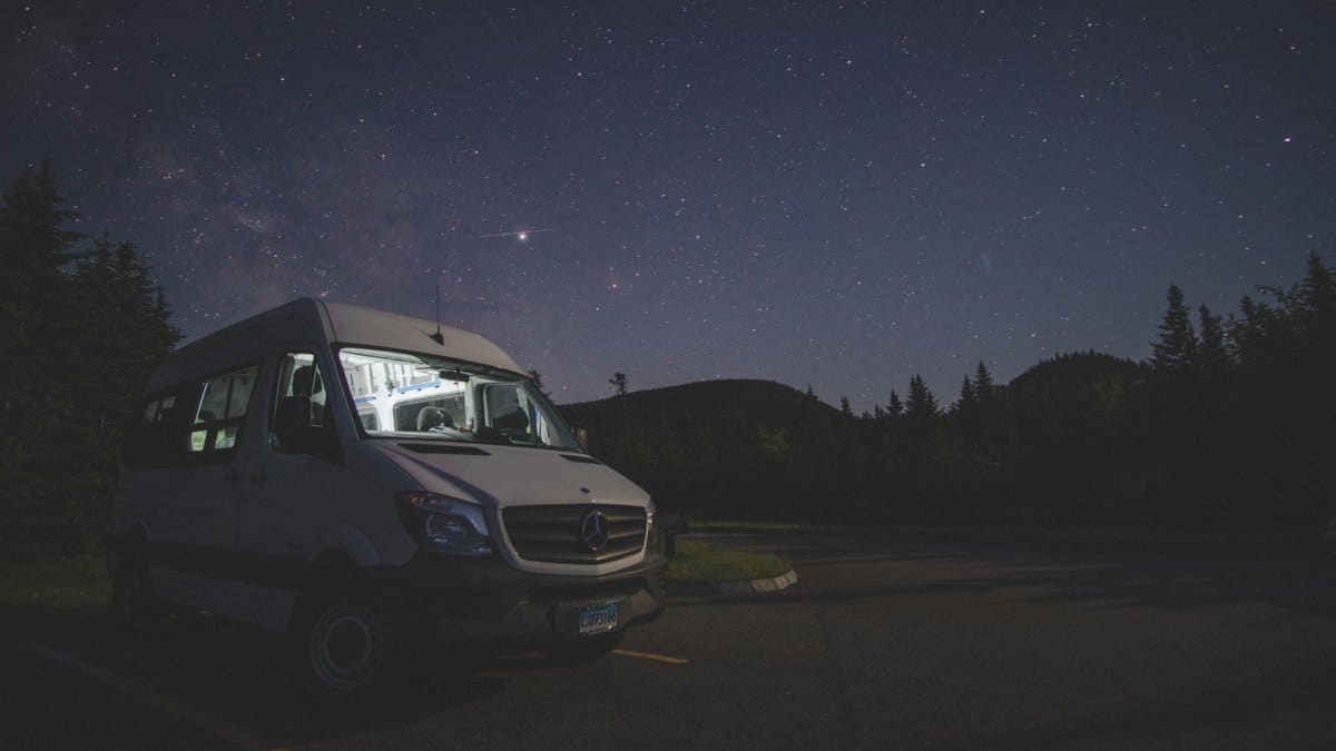 A camper van parked at night under a clear starry sky in a forested outdoor setting.