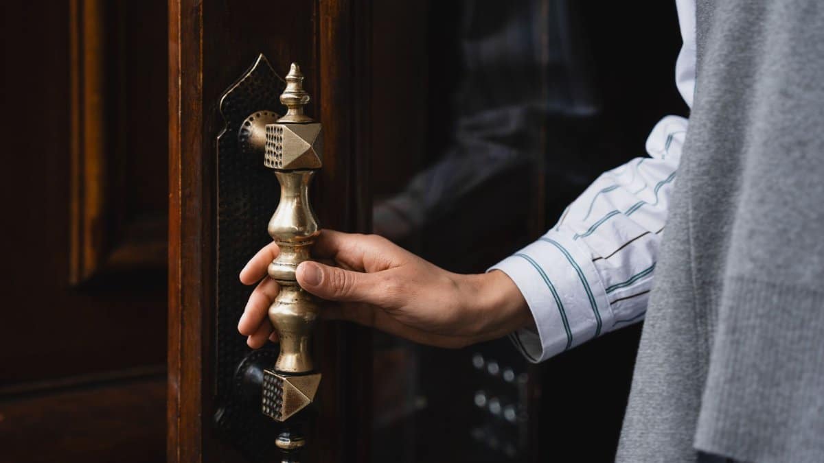 Close-up of a hand turning an ornate brass door handle, showcasing elegant craftsmanship.