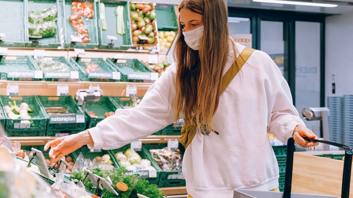 Woman wearing a face mask shopping for vegetables in a grocery store during the pandemic.