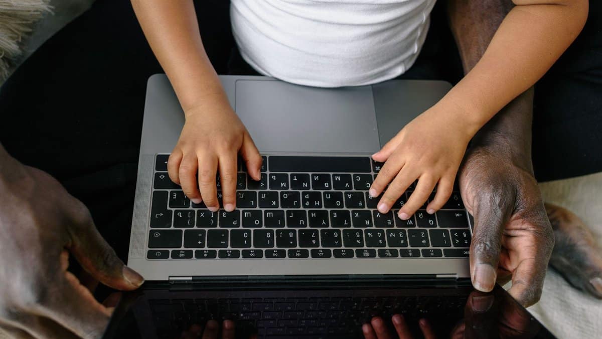 A child and adult using a laptop together, emphasizing learning and guidance.