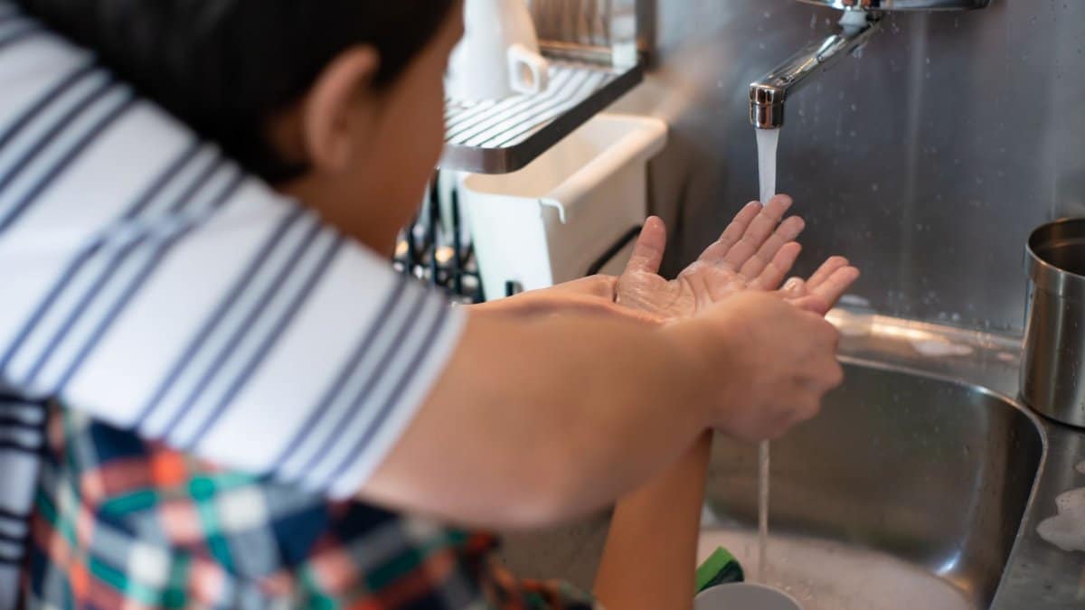 A child practicing hygiene by learning to wash hands under adult supervision at a kitchen sink.
