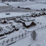 A snowy aerial view of a rural village with houses and fields in winter.