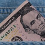 A five dollar bill tucked into a blue denim jeans pocket, symbolizing savings or cash on the go.