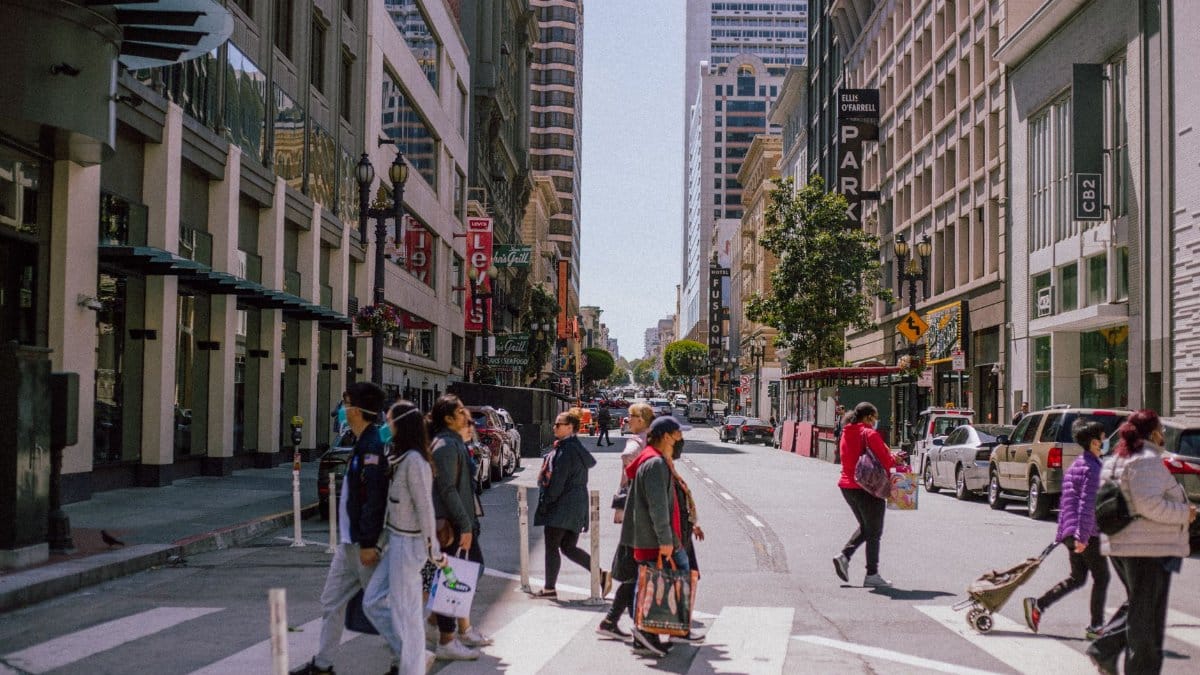 People crossing a city street at a bustling urban intersection during the day, showcasing modern architecture and city life.