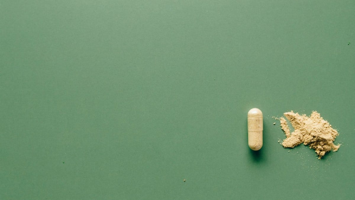 Close-up of herbal supplement capsule and powder on a minimalist green surface.