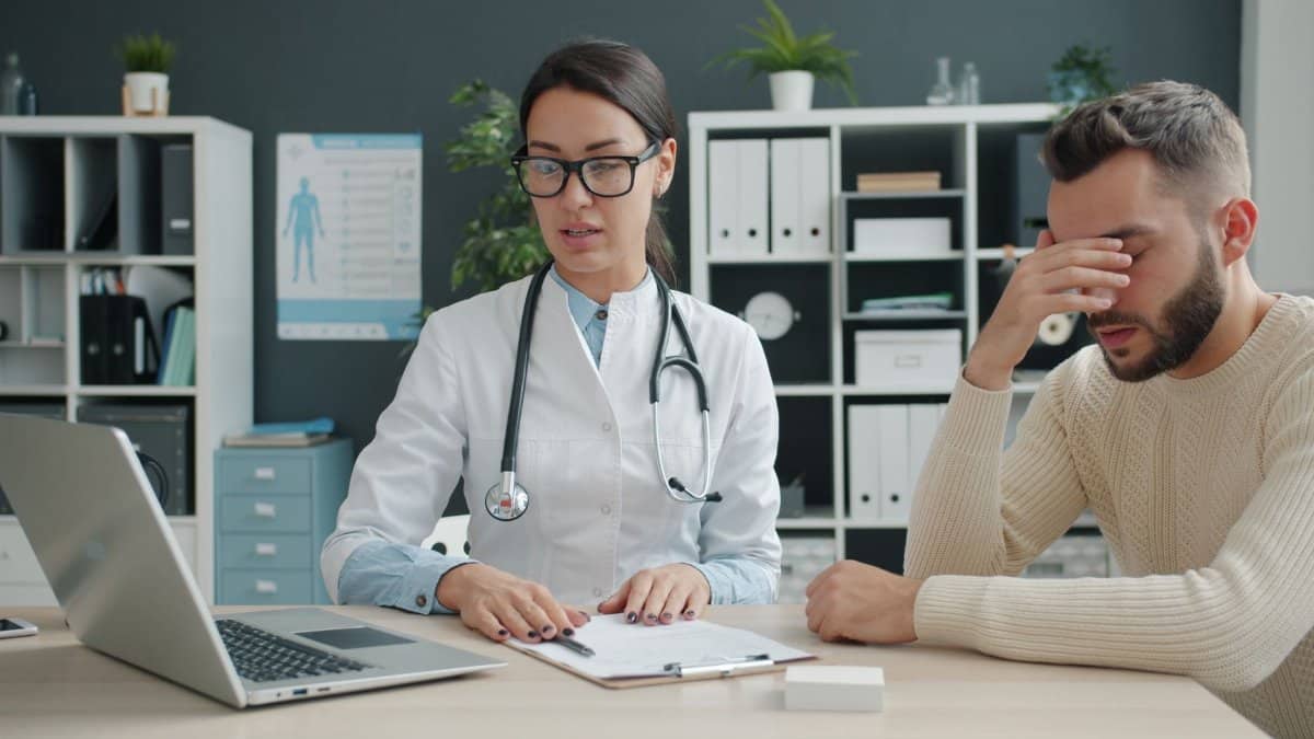 Healthcare professional discussing with patient in doctor's office. Stress and concern are evident.