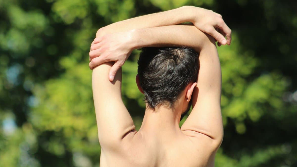 Man performs back stretching exercise on a sunny day, promoting wellness and fitness.