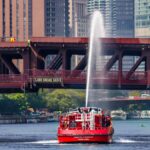 Fireboat sprays water under Lake Shore Drive bridge with Chicago skyline in the background.