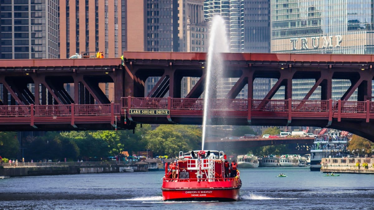 Fireboat sprays water under Lake Shore Drive bridge with Chicago skyline in the background.