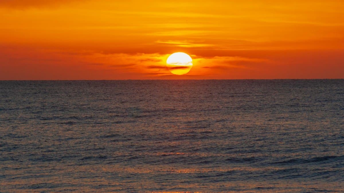 A breathtaking view of the sun setting over the ocean with rich orange and golden hues.