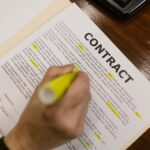 Focused view of a person highlighting text in a contract document on a wooden office desk.