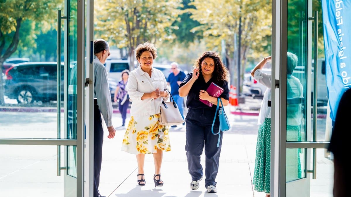A group of people walking into a building, smiling, on a sunny day.