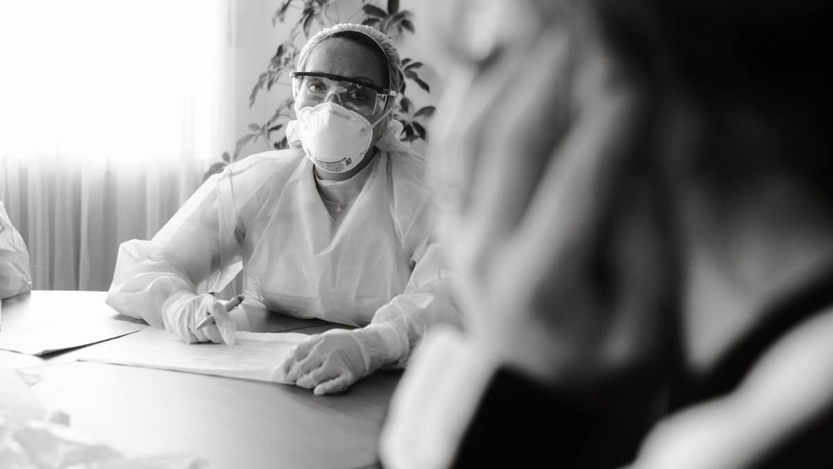 Healthcare professional in PPE speaking with a patient during a consultation, focusing on safety during health crises.