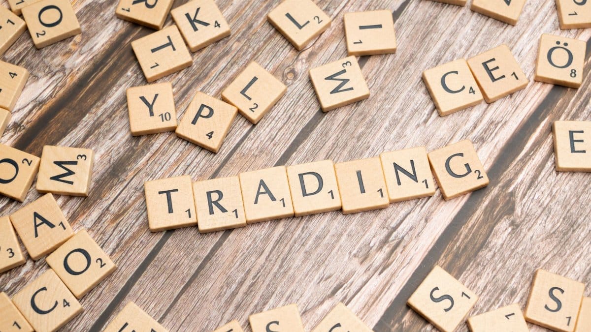 Wooden Scrabble tiles spelling 'TRADING' against a rustic wood background.