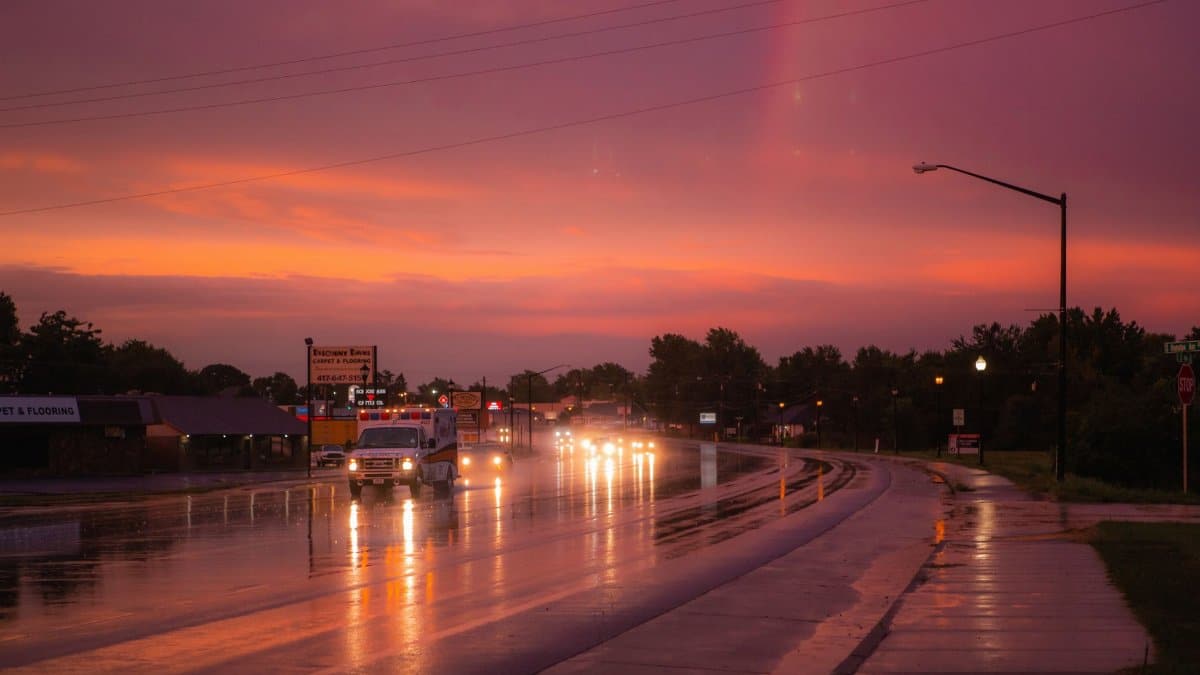 Vehicles navigate a rain-soaked highway at dusk under a vibrant sky.