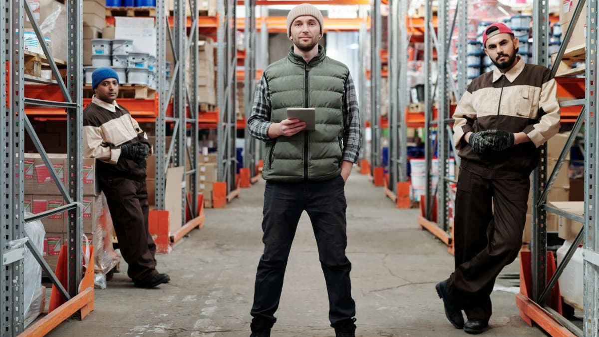 Three men in a warehouse standing among shelves with inventory.