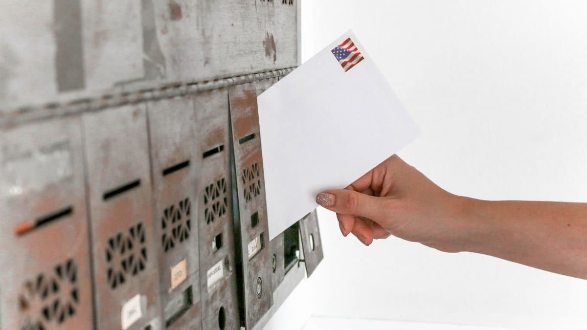 Close-up of a hand inserting a stamped envelope into a mailbox, symbolizing voting.