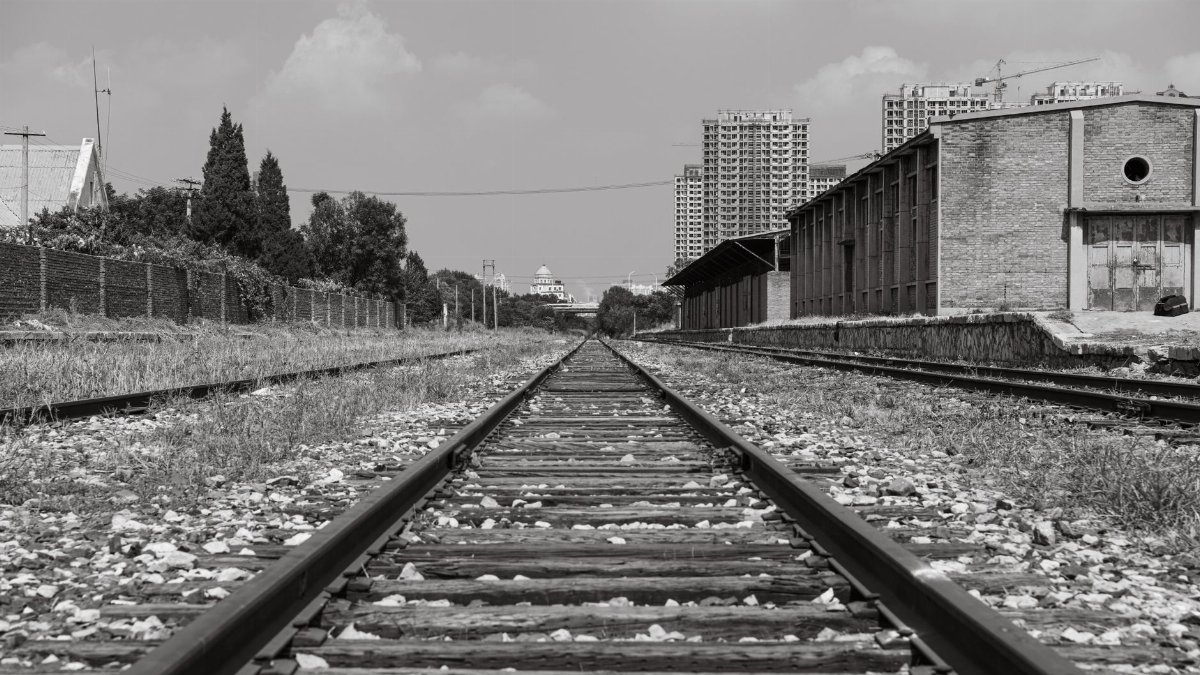 Black and white image of urban railway tracks leading towards city buildings.