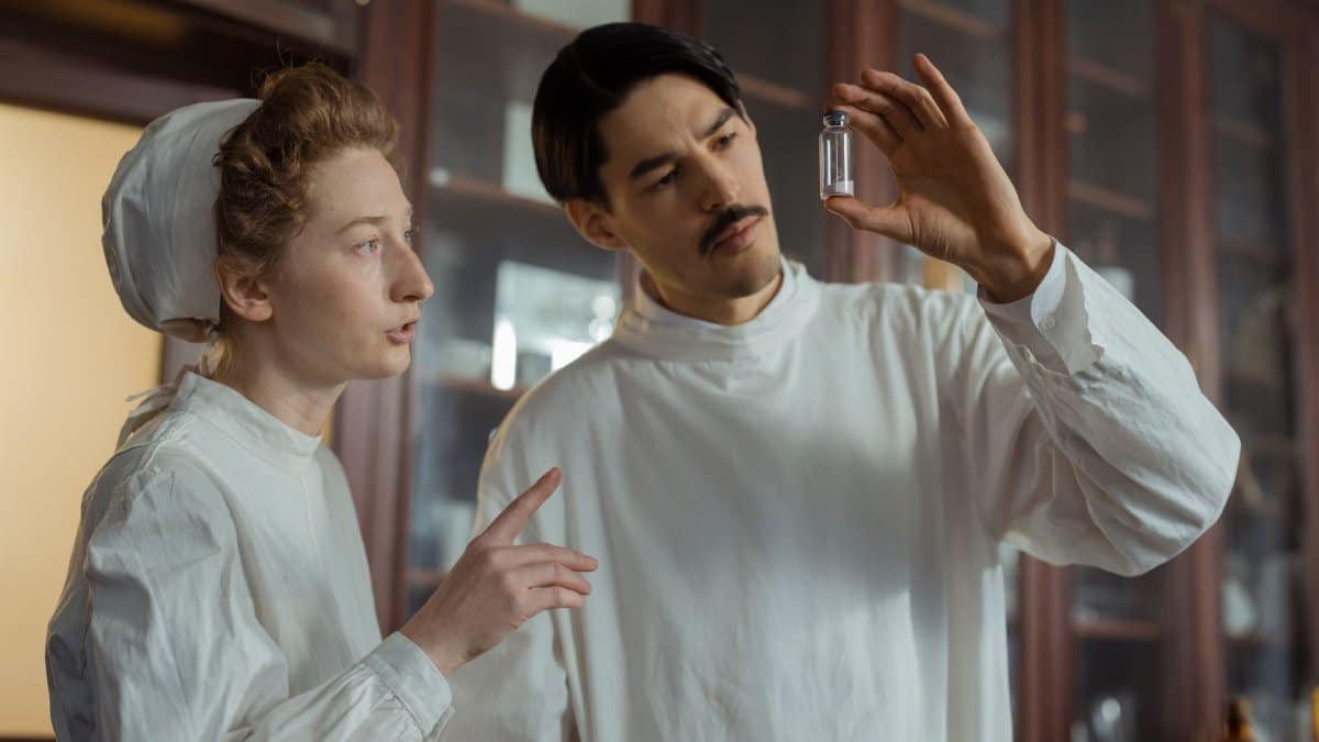 Researchers in a vintage laboratory examining a glass vial, showcasing historical scientific research.