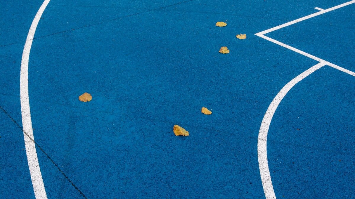 Vibrant blue sports court with white lines and scattered yellow leaves, showcasing abstract patterns.