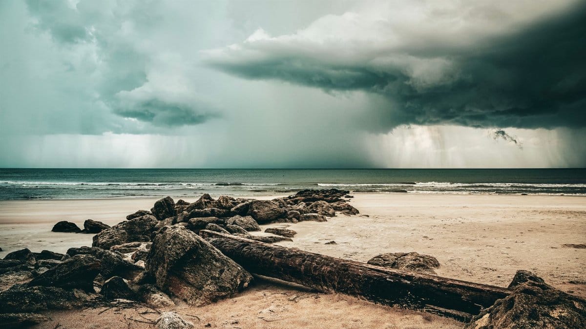A dramatic scene of a storm approaching a sandy beach with rocks under a cloudy sky.