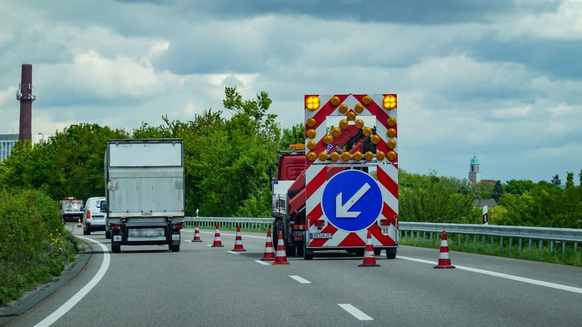 City highway under maintenance with traffic cones and warning signs directing vehicles.