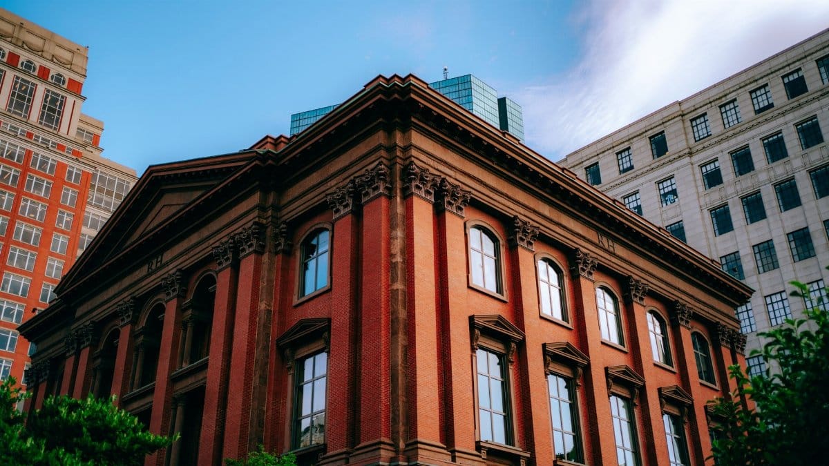 A Victorian red brick building in a bustling urban cityscape with a blue sky backdrop.