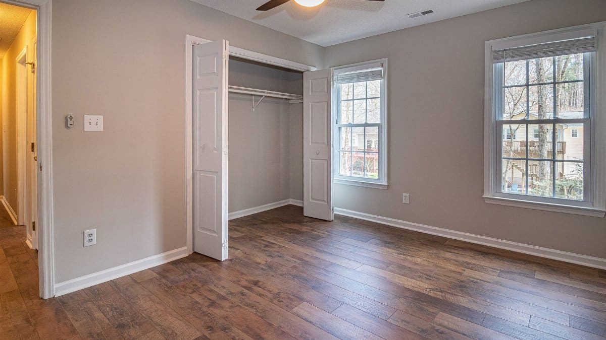 Spacious empty bedroom with wooden floor, ceiling fan, and open closet in a modern home.