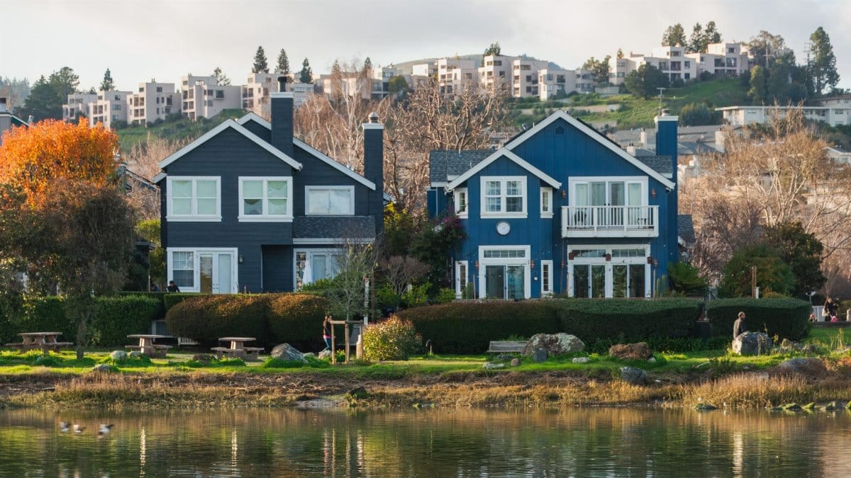 Beautiful row of waterfront homes surrounded by autumn trees reflecting in a calm river.