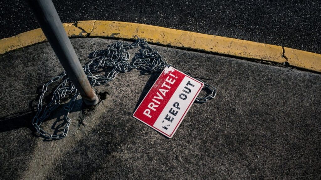 A chained 'Private Keep Out' sign lies on an urban sidewalk, emphasizing security.