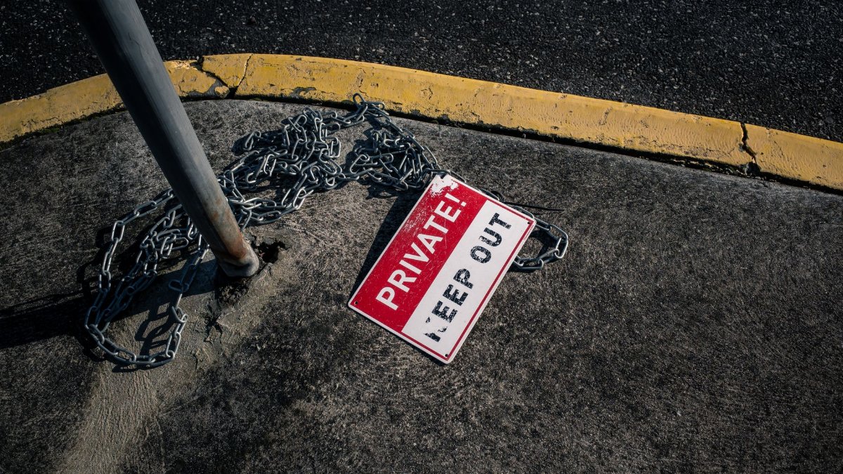A chained 'Private Keep Out' sign lies on an urban sidewalk, emphasizing security.