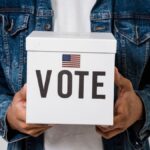 Person in denim holding a ballot box with a US flag, emphasizing voting rights.