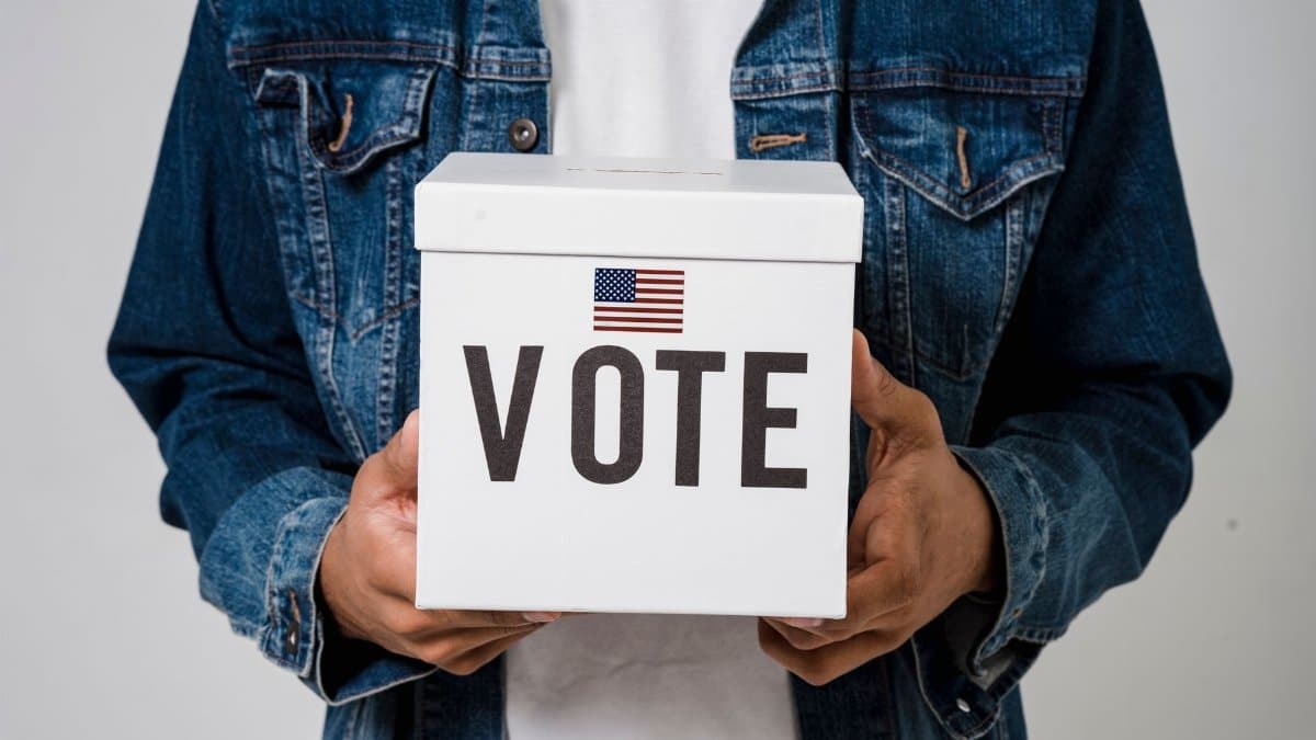 Person in denim holding a ballot box with a US flag, emphasizing voting rights.