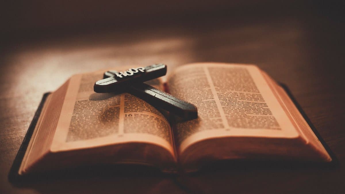 Close-up of an open Bible with a wooden cross inscribed with 'Hope' on a table.