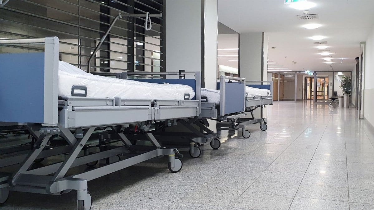 Quiet hospital hallway with neatly arranged empty medical beds under bright ceiling lights.
