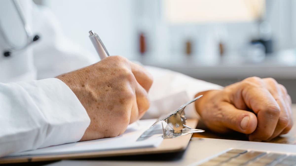 Close-up of a doctor writing notes on a clipboard in a well-lit office.