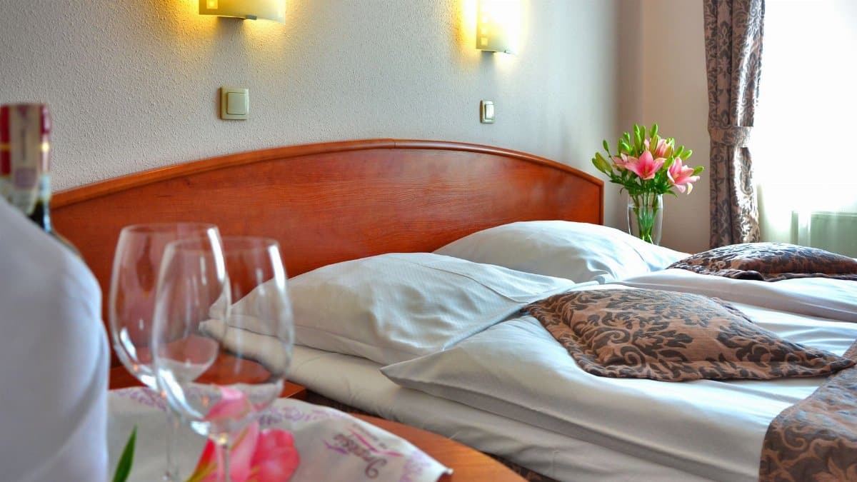 Elegant hotel room featuring a cozy bed, wine glasses, and floral decor, creating a welcoming atmosphere.
