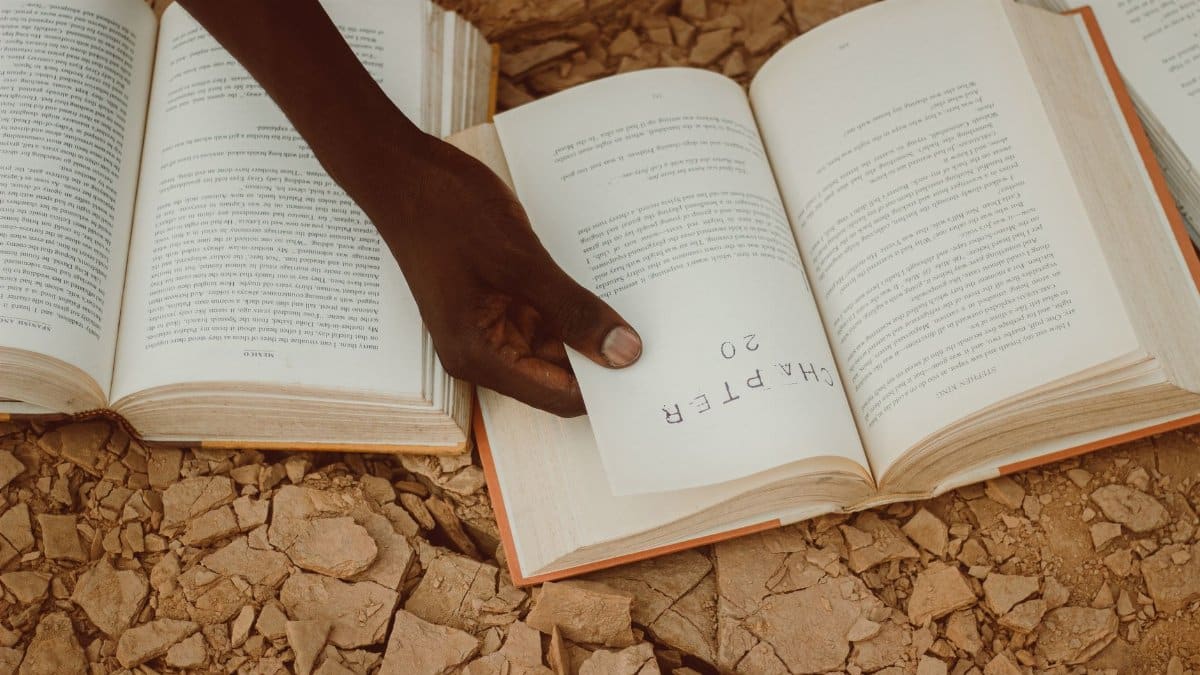 A person turning a page of a book set on a rocky surface, highlighting reading outdoors.