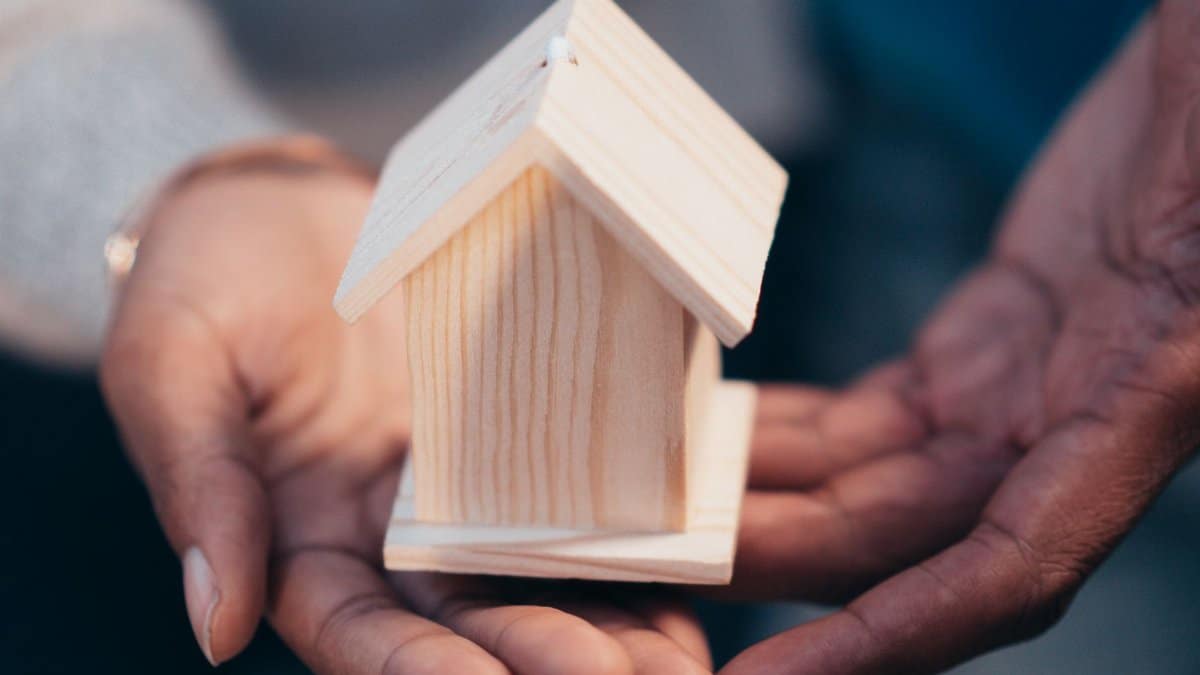 Close-up of hands holding a wooden house model representing real estate or new home purchase.