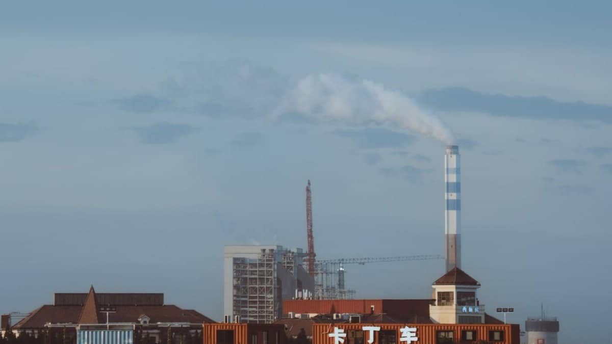 Factory with smokestack emitting smoke under a clear sky, industrial setting.