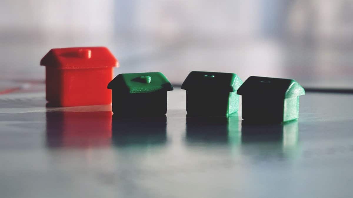 Close-up photo of red and green Monopoly game houses on a reflective surface.